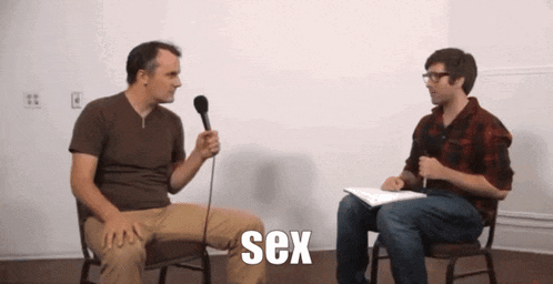 a man is sitting in a chair talking into a microphone and the word sex is visible