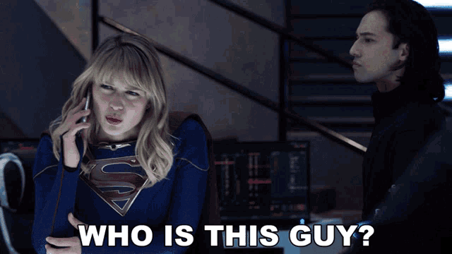 a woman in a superman costume is talking on a cell phone next to a man with the caption who is this guy
