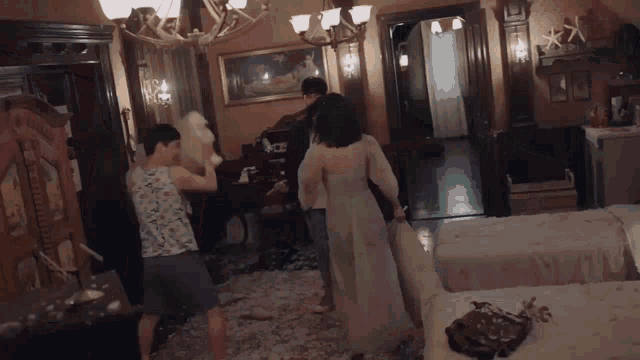 a group of people are having a pillow fight in a bedroom with two beds .