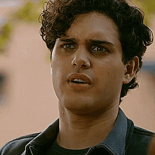 a young man with curly hair and braces on his teeth is wearing a denim jacket and a black shirt .