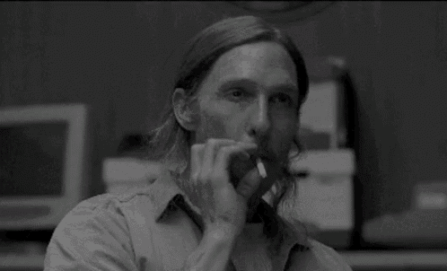 a man with long hair and a beard is smoking a cigarette and saying shee-it