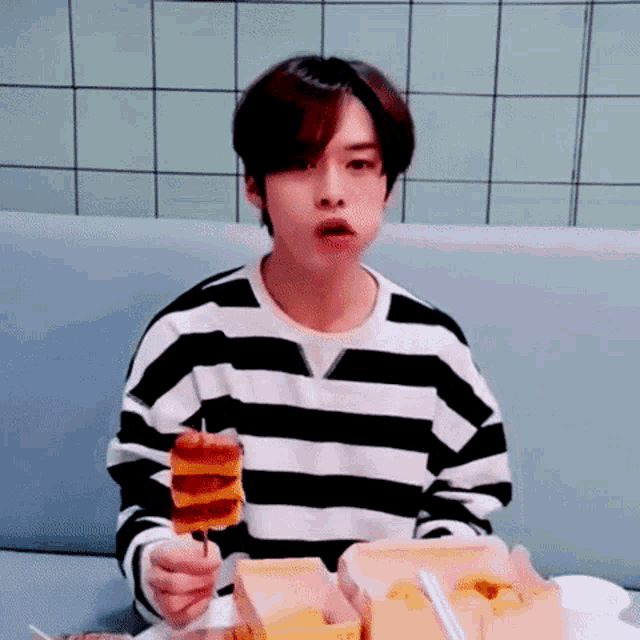 a young man in a black and white striped shirt is eating a sandwich on a stick .