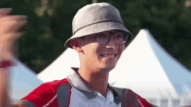 a man wearing a hat and glasses is smiling and waving .