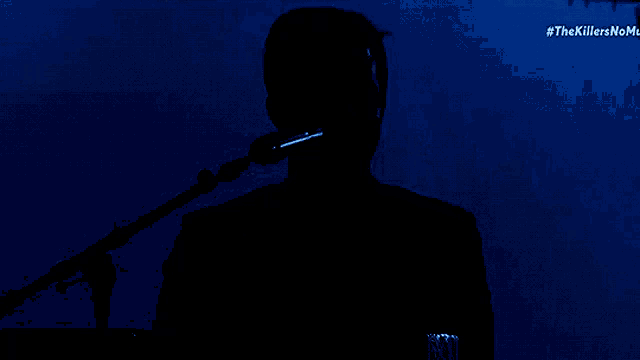 a silhouette of a man singing into a microphone with #thekillersnoname on the bottom right