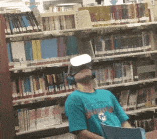 a man wearing a virtual reality headset sits in front of a bookshelf