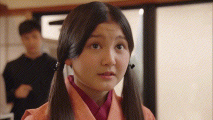 a girl with pigtails is looking at the camera with a man standing behind her .