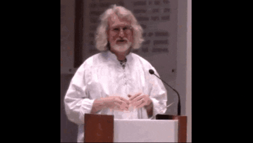 a man with glasses and a beard is standing at a podium giving a speech