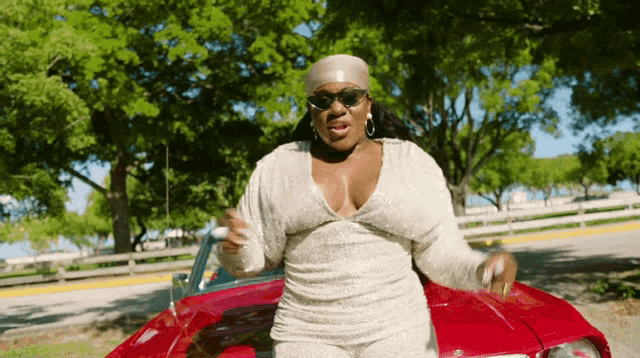a woman wearing sunglasses and a headband is standing next to a red car