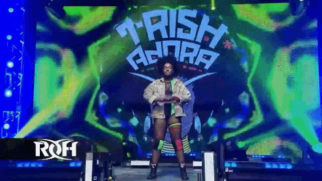 a wrestler named trish adora is standing in front of a large screen