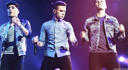 a group of young men are singing and dancing on a stage with a purple background that says one direction on it