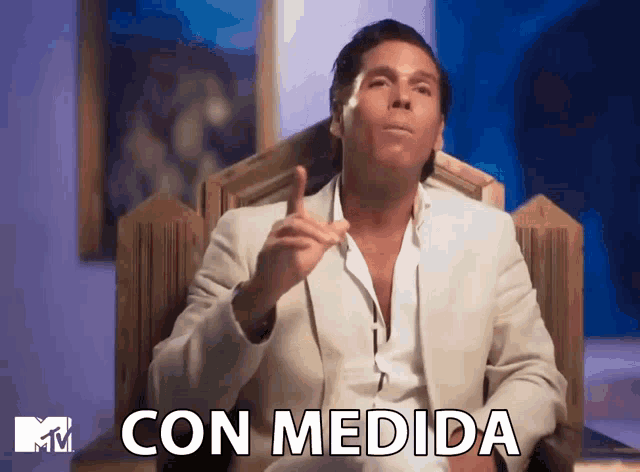 a man in a white suit sits in a chair with the words con medida written on the bottom