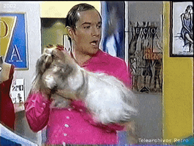 a man in a pink shirt is holding a dog in his arms