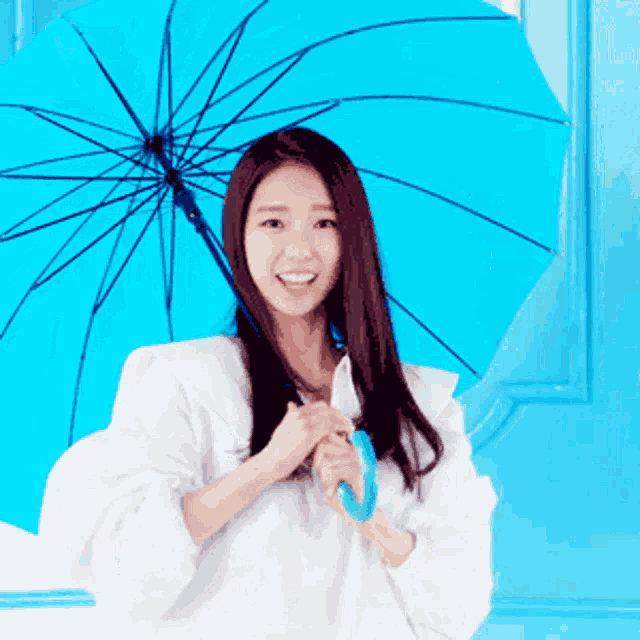 a woman is holding a blue umbrella in front of a blue wall