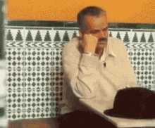 a man with a mustache is sitting at a table with a hat .