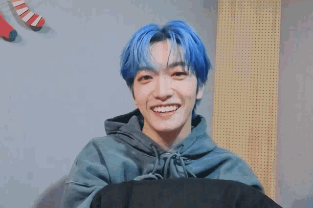 a young man with blue hair is smiling and holding his fist in the air