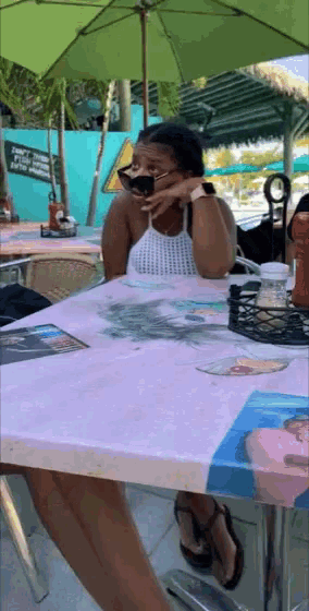 a woman sits at a table with a green umbrella