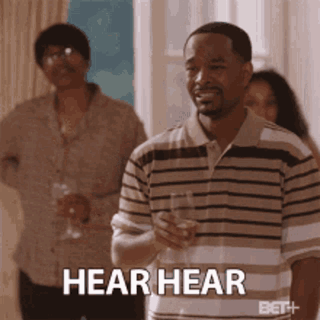 a man in a striped shirt is holding a glass and says hear hear