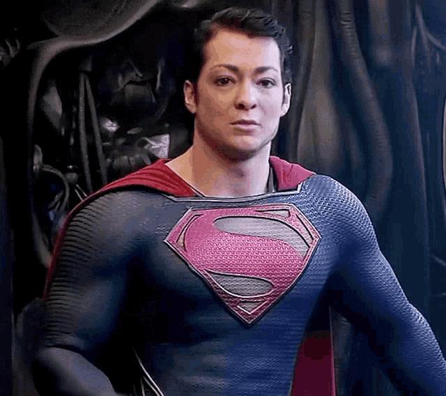 a man in a superman costume is standing in front of a black curtain and looking at the camera .