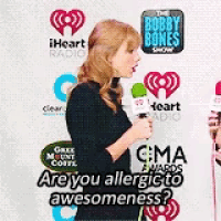 a woman is holding a microphone in front of a wall that says ' are you allergic to awesomeness ? '