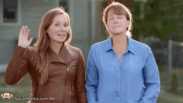 two women are standing next to each other and waving .