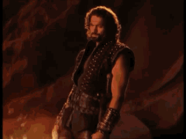 a man with a beard is standing in front of a fire with the words now you know below him