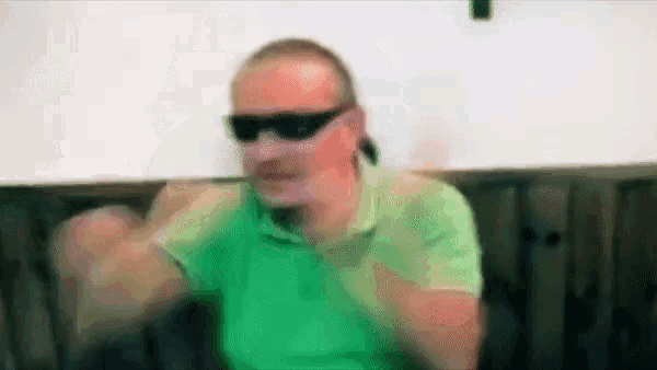 a man wearing sunglasses and a green shirt is sitting in a chair .