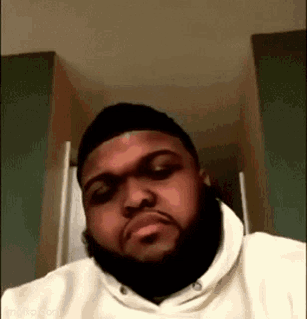 a man with a beard and a white hoodie is looking at the camera .