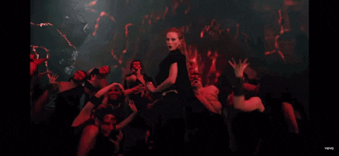 a woman in a black dress stands in front of a crowd of people wearing red masks