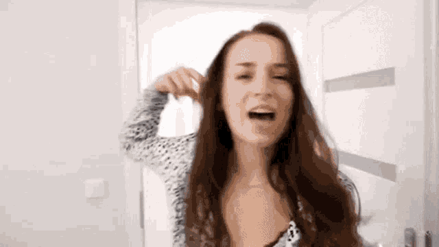 a woman is singing into a microphone while brushing her hair in a bathroom .