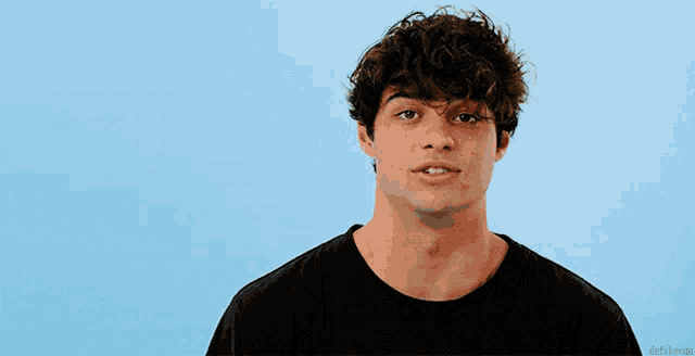 a man with curly hair is wearing a black shirt and looking at the camera