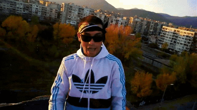 a man wearing sunglasses and a white adidas jacket