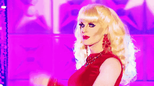 a drag queen wearing a red dress and blonde hair is standing on a stage .