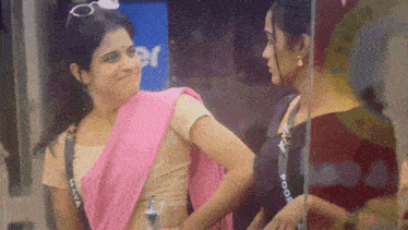 a woman in a pink saree is standing next to another woman in a black shirt that says poop