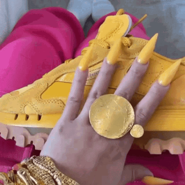 a woman 's hand with long yellow nails and a gold ring .