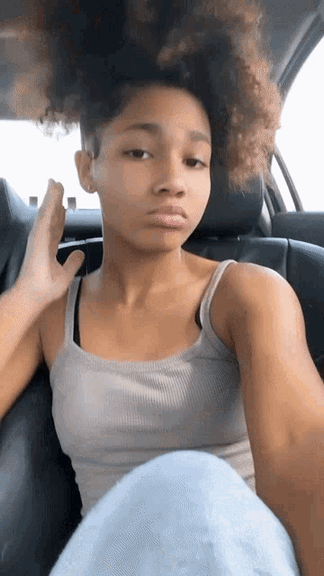 a young woman is sitting in the back seat of a car with her hand on her head .