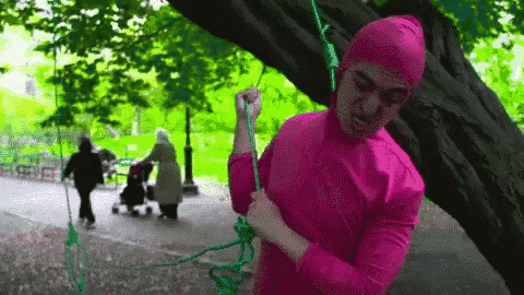 a man in a pink costume is swinging on a rope .