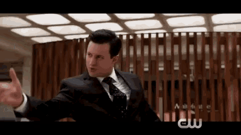a man in a suit and tie is standing in front of a wooden fence .