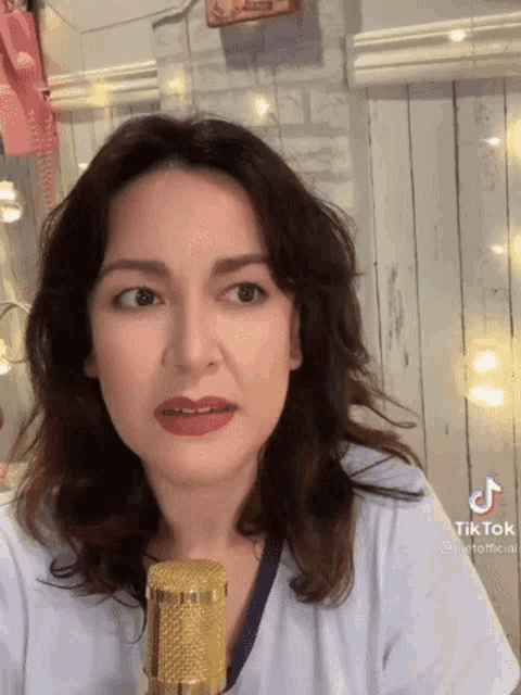 a woman is standing in front of a microphone and has a tik tok sticker on her face