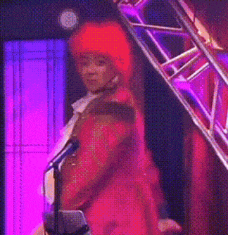 a man in a red hat is singing into a microphone on a stage