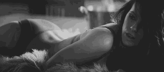 a black and white photo of a woman in lingerie laying on her stomach on a blanket .