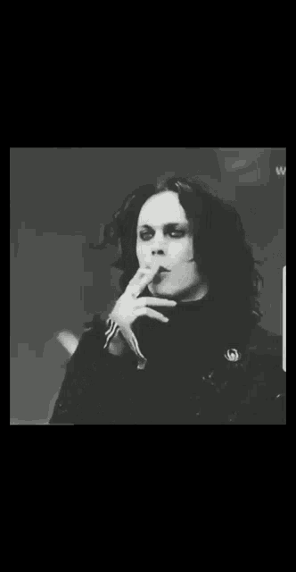 a black and white photo of a man with curly hair smoking a cigarette .