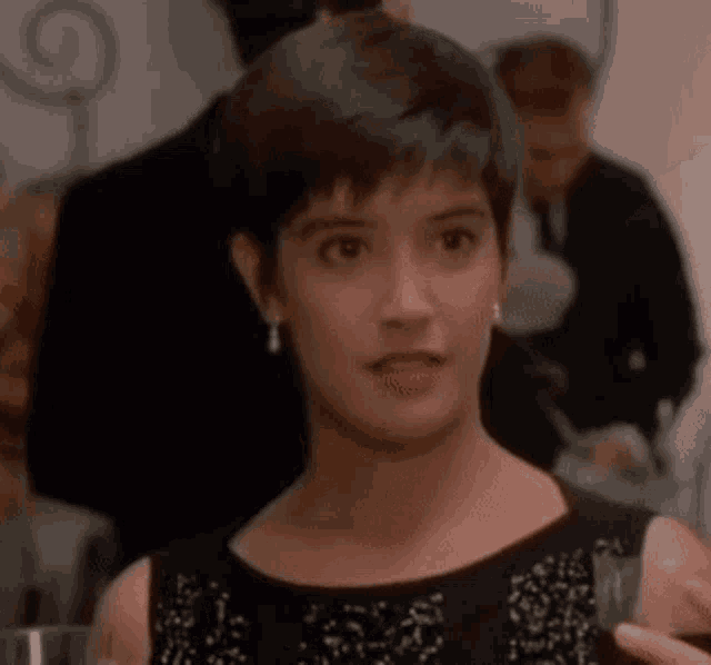 a woman in a black dress is holding a glass of wine in her hand .