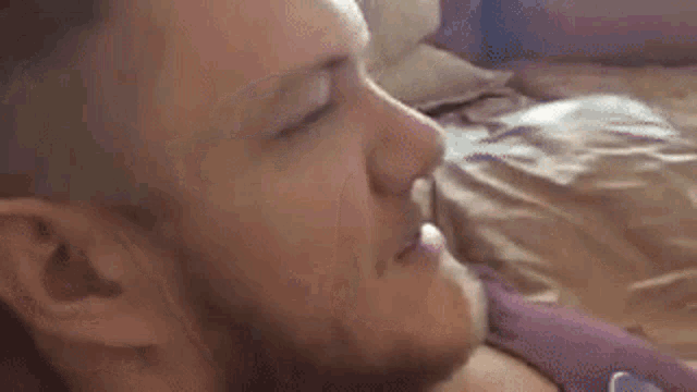 a man with a beard is laying on a bed with his eyes closed .