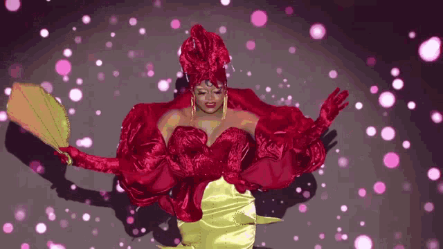 a woman in a red and yellow dress is dancing in front of a pink background .