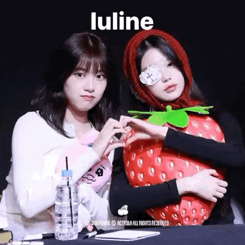 two girls are making a heart shape with their hands next to a strawberry .