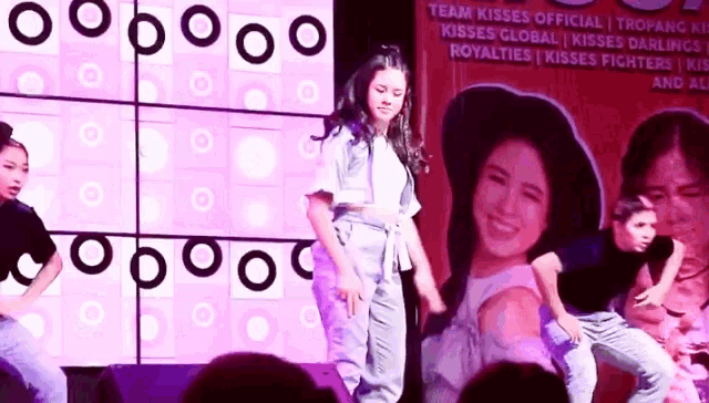 a girl is dancing on a stage in front of a large screen with a picture of a girl on it .