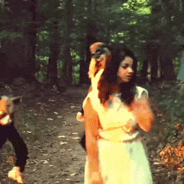 a woman in a white dress holds a cat on her shoulders in the woods