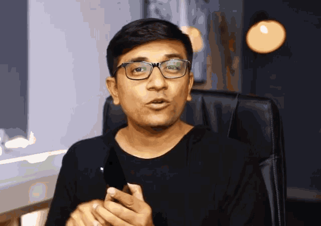 a man wearing glasses and a black shirt is talking on a phone