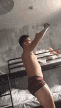 a man in underwear is standing on a bunk bed .