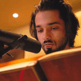 a man with a beard is reading a book in front of a black microphone